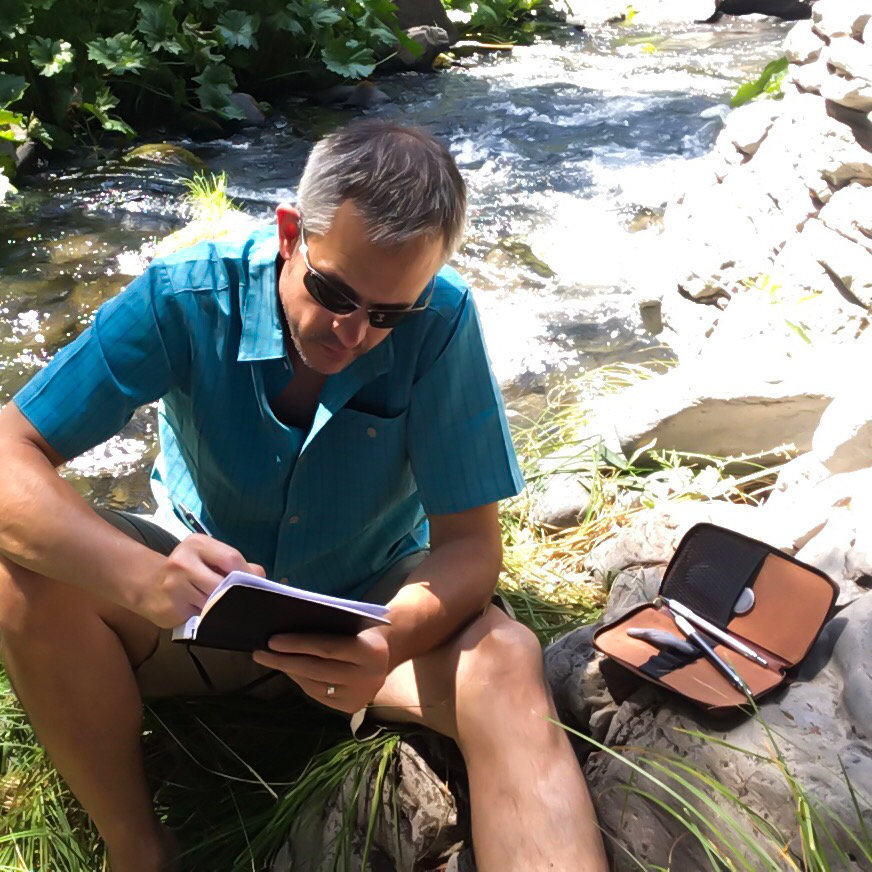 Man sketching by a river in the mountains